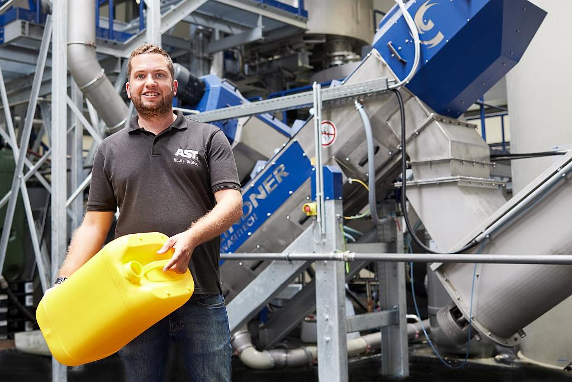 Hauke Grabau, Leiter des Bereichs Recycling bei der AST Kunststoffverarbeitung, vor der Lindner-Kunststoffrecycling-Anlage. In seinen Händen: einer der vielen AST-Kanister, die mit dem recycelten Granulat hergestellt werden. (Foto: Lindner)