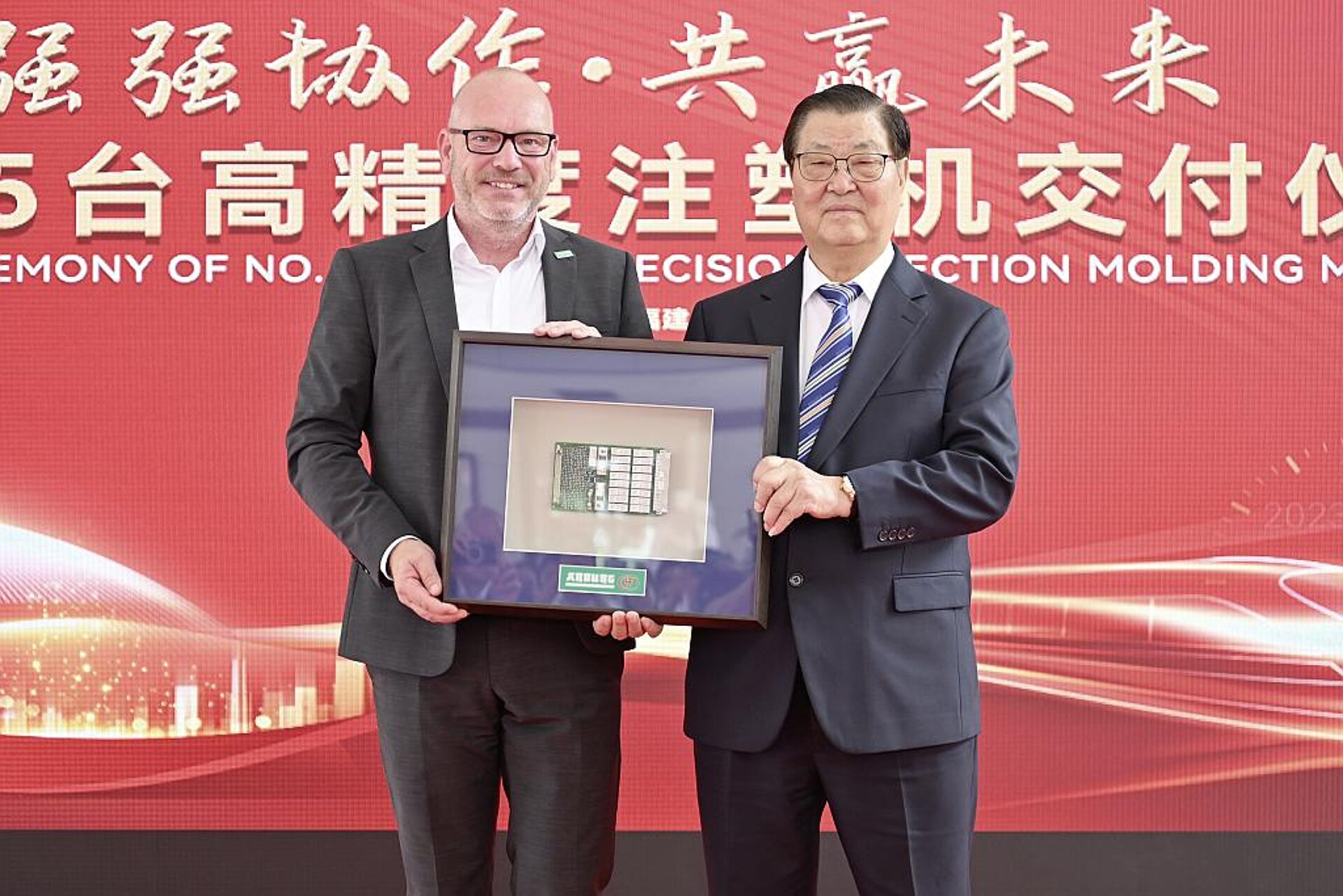 Stolz auf eine lange, enge Partnerschaft: Hongfa-Präsident Manjin Guo (r.) nimmt aus den Händen von Arburg-Geschäftsführer Technik, Guido Frohnhaus, die Platine eines Allrounders entgegen, die mit dem Relais von Hongfa bestückt ist. (Foto: Arburg)
