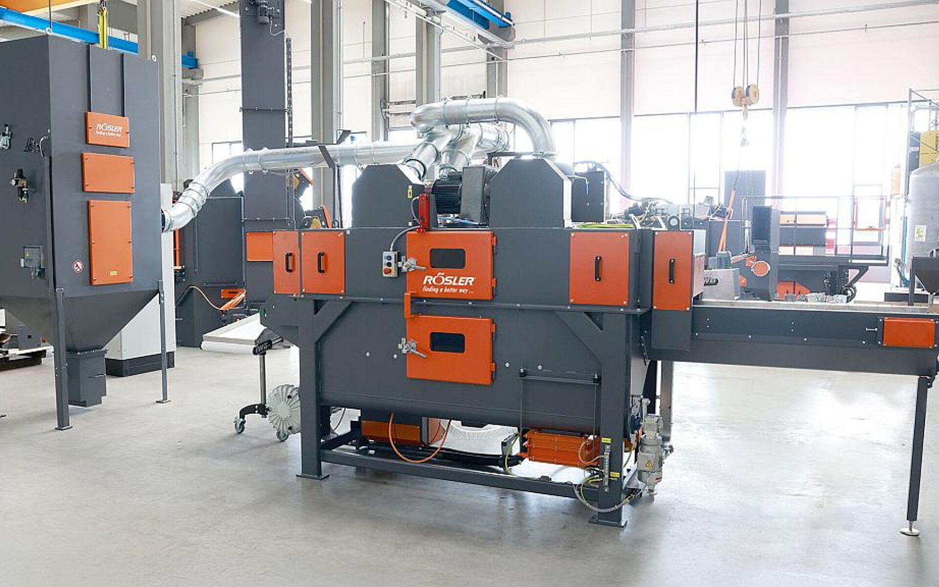 Durch den Einsatz der flexiblen Drahtgurt-Durchlaufstrahlanlage RSAB 370 T1+1 (Mitte) mit ATEX-konformem Filter (l.) konnte der Personaleinsatz für das Entgraten der Gehäuseteile nahezu halbiert werden. (Foto: Rösler Oberflächentechnik)